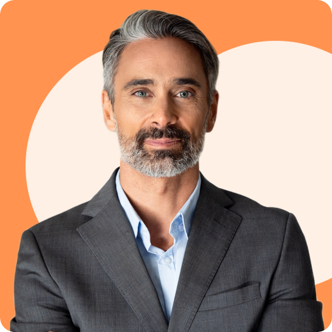 A middle-aged man with gray hair and a beard, wearing a gray suit and blue shirt, stands against an orange and cream background.