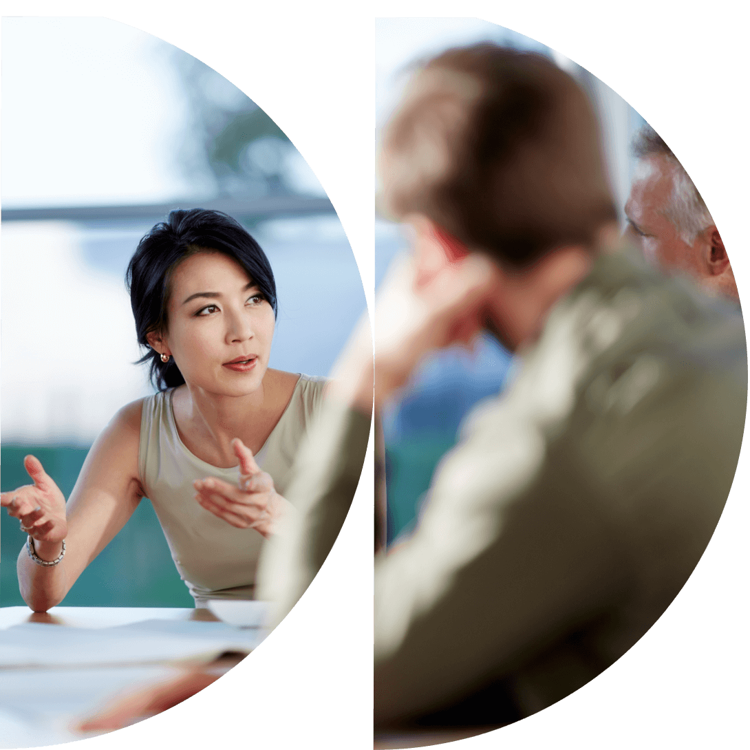 A woman is gesturing while talking to two people at a table in an office setting.